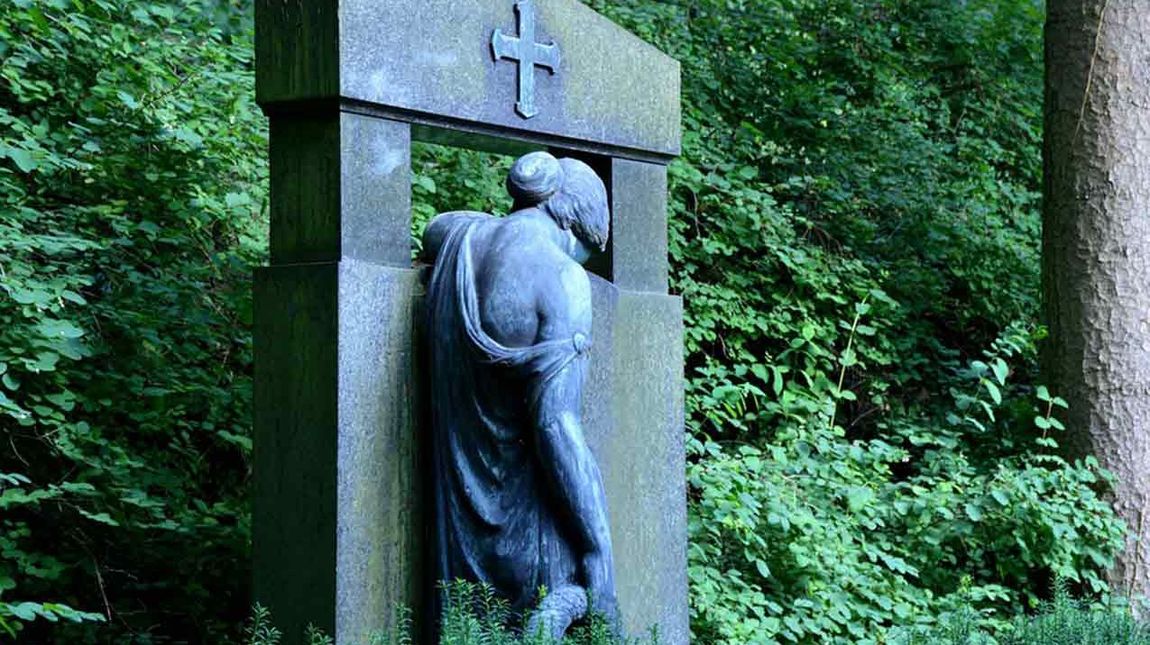 Statue einer Frau, die sich an einem Grabstein festhält